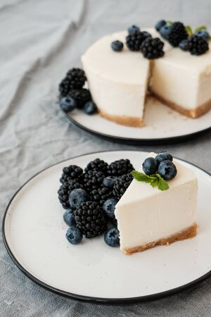 cheesecake New York with fresh berries and a slice on a plate decorated with blueberries and blackberries. Grey background. Minimalism. Delicious breakfast conceptionの写真素材