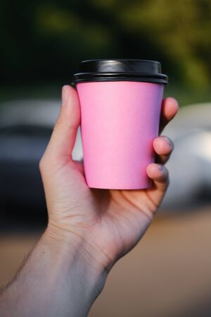 Pink paper coffee cup with a black cap in a male hand on a green background. Coffee to go, take-away coffee.の写真素材