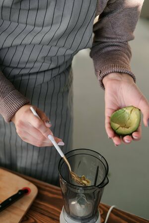 Female hands holding a spoon and half fresh ripe avocado. Healthy eco food. The product of organic...