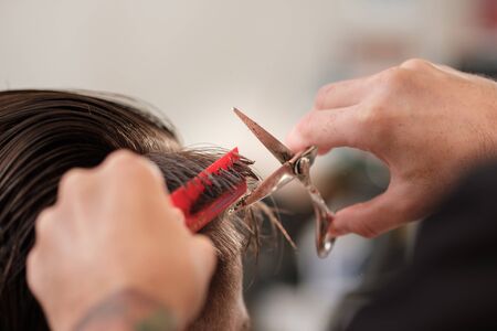 Hairdressing services. A man cuts hair at a hairdresser-stylist in a barbershop. scissors comb close-upの写真素材