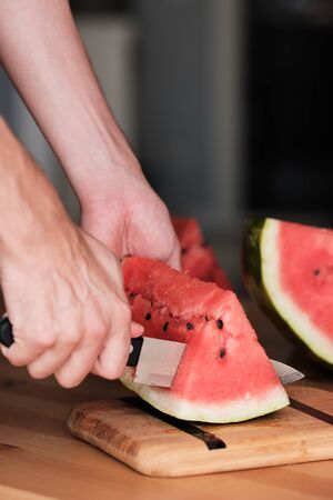 Hands chop watermelon with a knife on a bamboo cutting board. side viewの写真素材