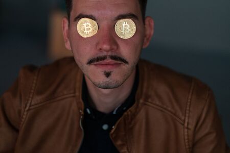 young man with bitcoins in the eye sockets on a dark background. financier. business meeting. mafiaの写真素材