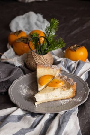 persimmon cheesecake on a dark background. Pieces of cake decorated with persimmons and Christmas tree branches. top viewの写真素材