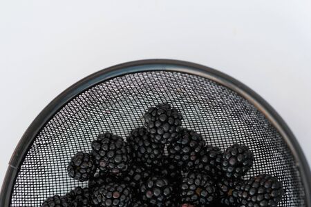 Top view of wet metal strainer full of washed out blackberries isolated on white background.close-up