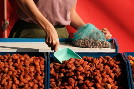 Dried fruit seller. young woman imposes dried apricots and weighs it for the buyer.super foodの写真素材