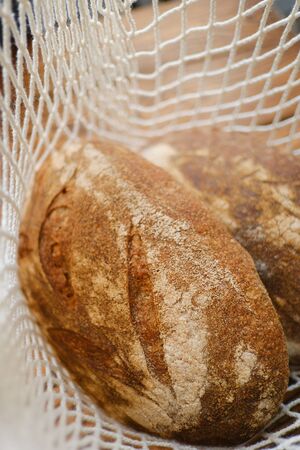Different buns of fresh bread in wicker string bag. Freshly baked wheat bread, still life with...