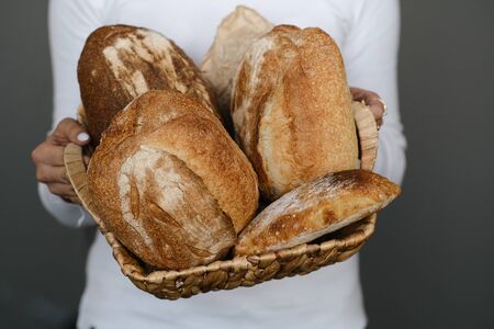 Hands Of A Baker Hold A wicker basket With Different Homemade Loaf Of Bread Rustic. Bakery employee...