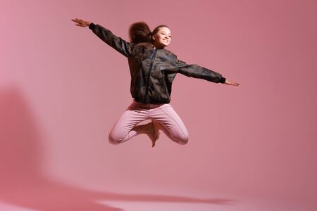 Portrait of cheerful positive girl jumping in the air with raised fists looking at camera isolated...