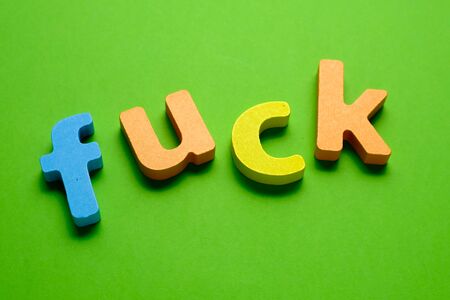 Word FUCK made of color wooden letter, isolated on green background. Learning the English alphabet...