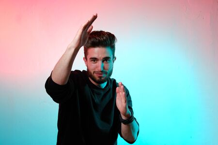 Beautiful caucasian young man portrait isolated on multicolored neon light backgroud. Young, smiling, surprised, screaming. Human emotions, facial expression concept. Trendy colors.Advertising conceptの写真素材