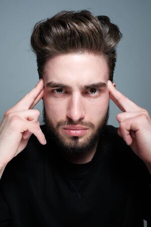 A young dark-haired man with a beard holds his head and shows different human emotions: hatred,...