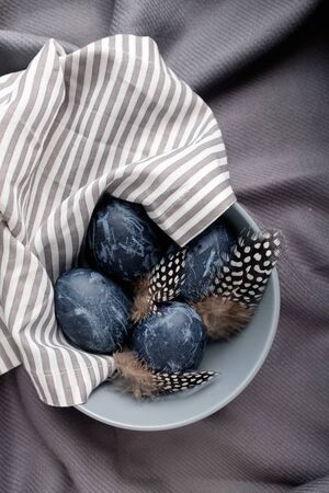 Naturally dyed blue eggs prepared for Easter on gray texture tablecloth background. Happy Easter. Easter background with Easter eggs and feathers in a ceramic gray bowl. Background with easter eggs.の写真素材