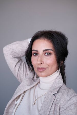 Portrait of a smiling mid-aged business woman (30-35 years old) with dark hair and brown eyes in a milk-colored trouser suit and turtleneck against a light wall. Close-up portrait of a businesswomanの写真素材