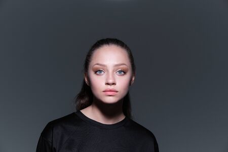 A close-up portrait of a young beautiful serious girl with blue eyes and brown hair in a black...