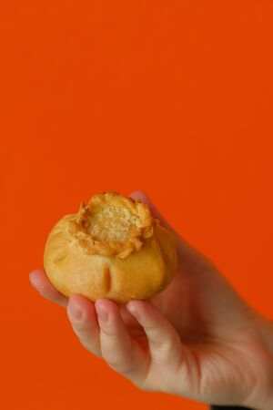 Gubadia in hand on an orange background. Traditional Tatar Cuisine.Tatar pie Gubadia, delicious pastry with cottage cheese and raisins. Traditional food, quick snack of dough.の写真素材