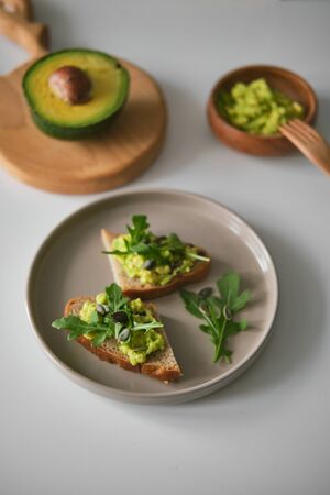 Toast with avocado, arugula and pumpkin seeds on a plate and avocado on wooden board in the shape of deer antlers. Bowl with guacamole. The concept of a healthy breakfast and diet. Top viewの写真素材