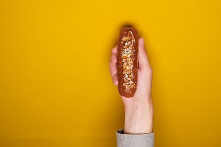 Tasty eclair in hand on a gray or yellow background. Food in the style of minimalism. People lifestyle concept. Mock up copy space.の写真素材