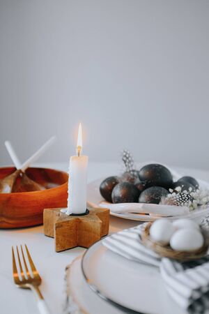 Rustic easter table setting with eggs. Easter table setting with white plate, gray textile napkin, candles, quail and chicken eggs and blossom branch on table. Mock up easter cardの写真素材