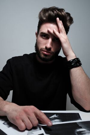 A young dark-haired man with a beard holds his head and shows different human emotions: hatred, fear, despair, horror, malaise, headache, clairvoyance. Close-up studio portrait of a man.の写真素材