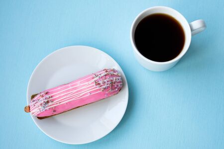 Tasty eclair, a cup of black coffee and a cactus on a blue background. Food in the style of minimalism. Breakfast concept. Modern breakfast. People lifestyle concept. Mock up copy space.の写真素材