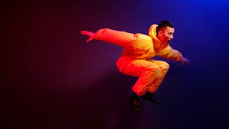 An Asian man in a yellow chemical protection suit screams in a jump on a colored trend background....