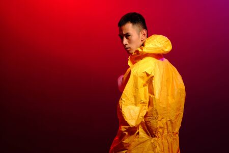 Asian man in a yellow suit of chemical protection on a colored trendy background. Fashion shooting in Asian style, neon lights and fashionable clothes, professional model. Coronavirus Protection.の写真素材