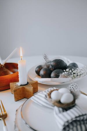 Rustic easter table setting with eggs. Easter table setting with white plate, gray textile napkin, candles, quail and chicken eggs and blossom branch on table. Mock up easter cardの写真素材