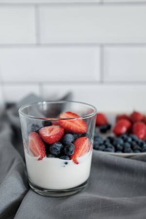 Delicious dessert: natural yogurt in a glass cup with fresh berries, strawberries and blueberries. Rustic breakfast in the kitchen. Kinfolk style lifeの写真素材