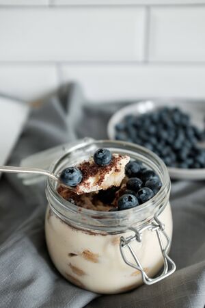 Delicious dessert: tiramisu in a glass jar and natural yogurt in a glass cup with fresh berries, strawberries and blueberries. Rustic breakfast in the kitchen. Kinfolk style lifeの写真素材