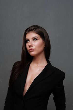 Close-up portrait of a beautiful cute girl with long hair and in a black jacket on a gray background. Girl posing for the photographer in a photo studio.の写真素材