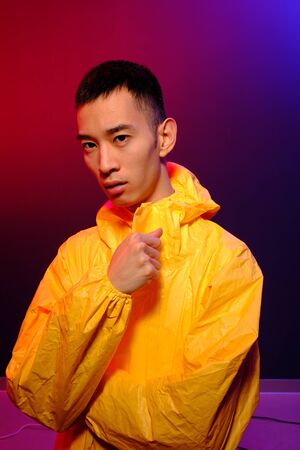 Asian man in a yellow suit of chemical protection on a colored trendy background. Fashion shooting in Asian style, neon lights and fashionable clothes, professional model.の写真素材