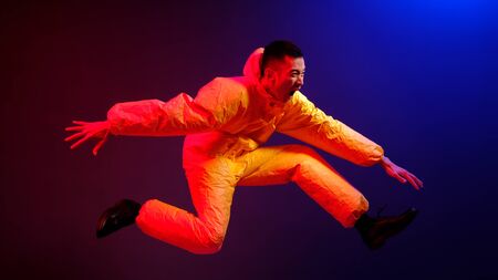 An Asian man in a yellow chemical protection suit screams in a jump on a colored trend background....