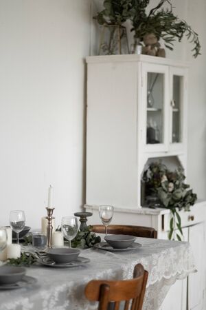 Table setting: gray dishes, white candles, candlesticks, glass goblets, sprigs of eucalyptus on a wooden table with a white tablecloth. Beautiful Scandinavian style interior.の写真素材