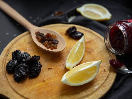 Products on a round wooden board: lemon slices, prunes, broccoli and dried grapes (raisins) in a wooden spoon. Ingredients for cooking.の写真素材