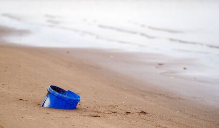 Blue plastic bucket in the sand on the beach. Pollution of the environment and the oceans. Microplastic in the ocean. Pollution and recycling conceptの写真素材