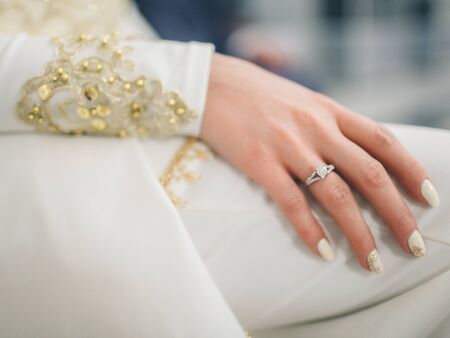 Bride hand with beautiful diamond ring on white dress. Hands close up. Wedding day. Exchange of rings and vows.の写真素材