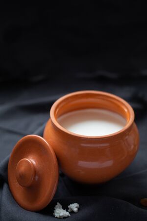 Brown ceramic pot with sour cream and a wooden spoon with raisins (dry grapes) on a dark background. Healthy food, dairy products. Farm Products Conceptの写真素材