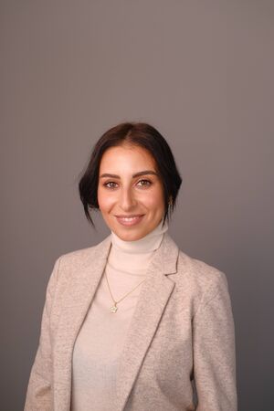 Portrait of a smiling mid-aged business woman (30-35 years old) with dark hair and brown eyes in a milk-colored trouser suit and turtleneck against a light wall. Close-up portrait of a businesswomanの写真素材