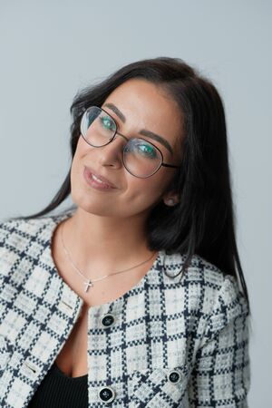 Portrait of a smiling mid-aged business woman (30-35 years old) with dark hair and brown eyes in glasses for vision and a jacket against a light wall. Close-up portrait of a businesswoman.の写真素材