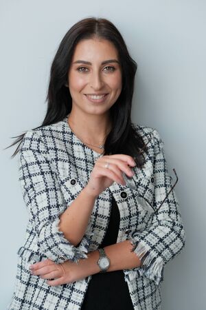 Portrait of a smiling mid-aged business woman (30-35 years old) with dark hair and brown eyes in glasses for vision and a jacket against a light wall. Close-up portrait of a businesswoman.の写真素材