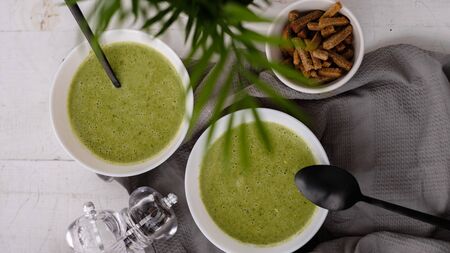 Spring detox broccoli green cream soup in white plates, bowl with crackers and stylish black cutlery on grey background. Clean eating, dieting, vegan, vegetarian, healthy food conceptの写真素材