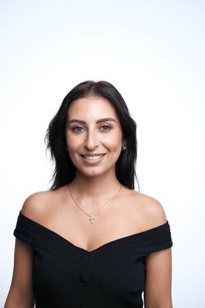 A large portrait of a smiling middle-aged woman (30-35 years old) with dark hair and brown eyes in a black dress on a light background. Portrait of happy young woman in black dress on grey backgroundの写真素材