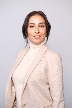 Portrait of a smiling mid-aged business woman (30-35 years old) with dark hair and brown eyes in a milk-colored trouser suit and turtleneck against a light wall. Close-up portrait of a businesswomanの写真素材