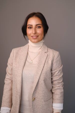 Portrait of a smiling mid-aged business woman (30-35 years old) with dark hair and brown eyes in a milk-colored trouser suit and turtleneck against a light wall. Close-up portrait of a businesswomanの写真素材