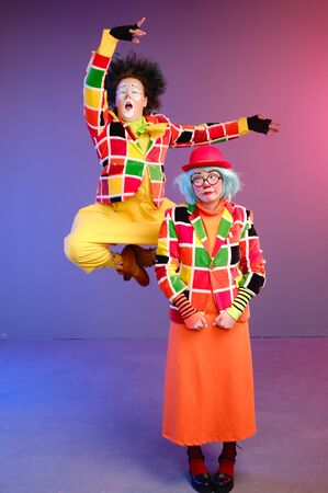 Two clowns a man and a woman with makeup in bright colored costumes are fooling around and showing a presentation using various accessories. April Fools Day concept. Birthday for kidsの写真素材