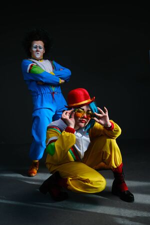 Two clowns a man and a woman with makeup in colored tracksuits in the style of the 80s or 90s posing against a trendy neon background.Party disco 80s 90s vibes.Creative art purple color styleの写真素材