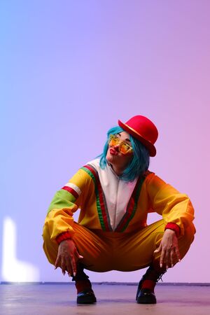 Clown woman with makeup in colored tracksuits in the style of the 80s or 90s posing against a trendy neon background.Party disco 80s 90s vibes.Creative art purple color styleの写真素材