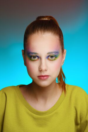Close-up portrait of a beautiful young girl in a green knitted dress with bright color makeup on a blue backgroundの写真素材