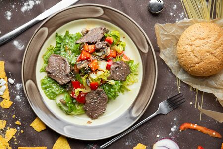 Beef steak salad with cherry tomatoes, cucumbers, red onions, romaine salad and lime mustard olive oil salad dressing on dark background, top viewの写真素材