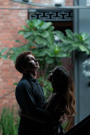 Young beautiful couple - a girl in a magnificent dress and a guy in a black shirt and trousers are in a building with a beautiful interior and high glass ceilings. Concept of romance and loveの写真素材